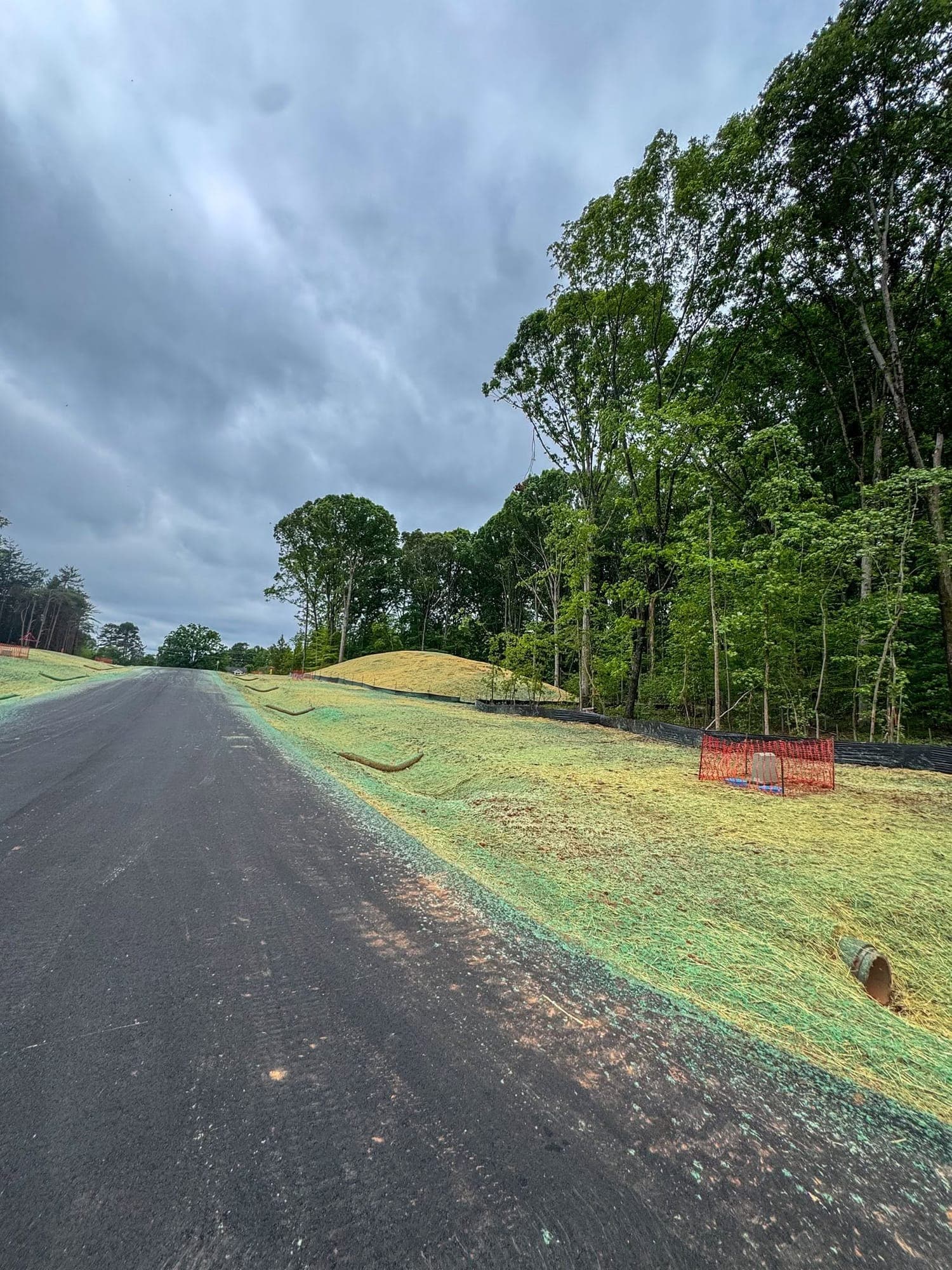 Freshly seeded and strawed roadside slope with wattles and silt fence along a new subdivision road