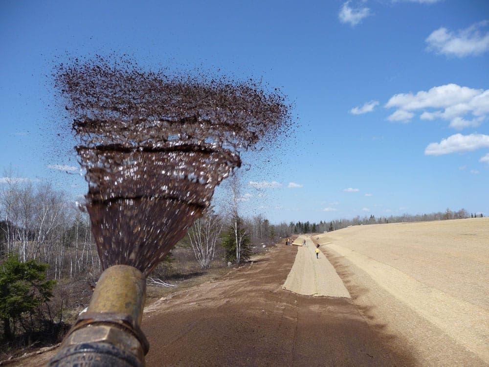 Hydroseed slurry being sprayed from a truck-mounted hose along a graded roadway shoulder